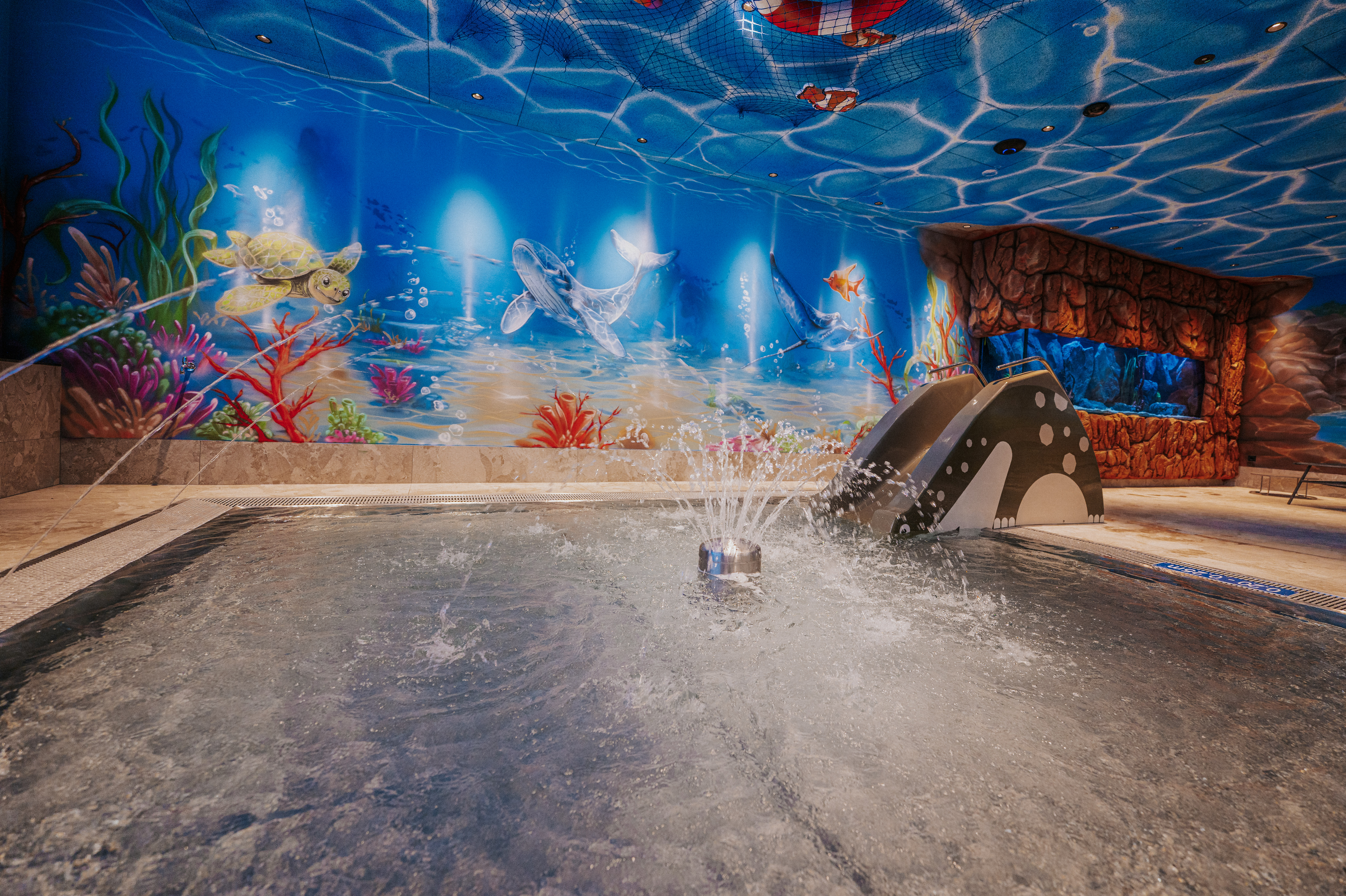 Wohnmobilstellplatz: Farbenfroher Wasserspielbereich mit Rutsche, Wasserspielen und faszinierender Unterwasserwelt in der IKUNA Spa- und Wellnesswelt. - IKUNA CAMPING RESORT + Naturerlebnispark