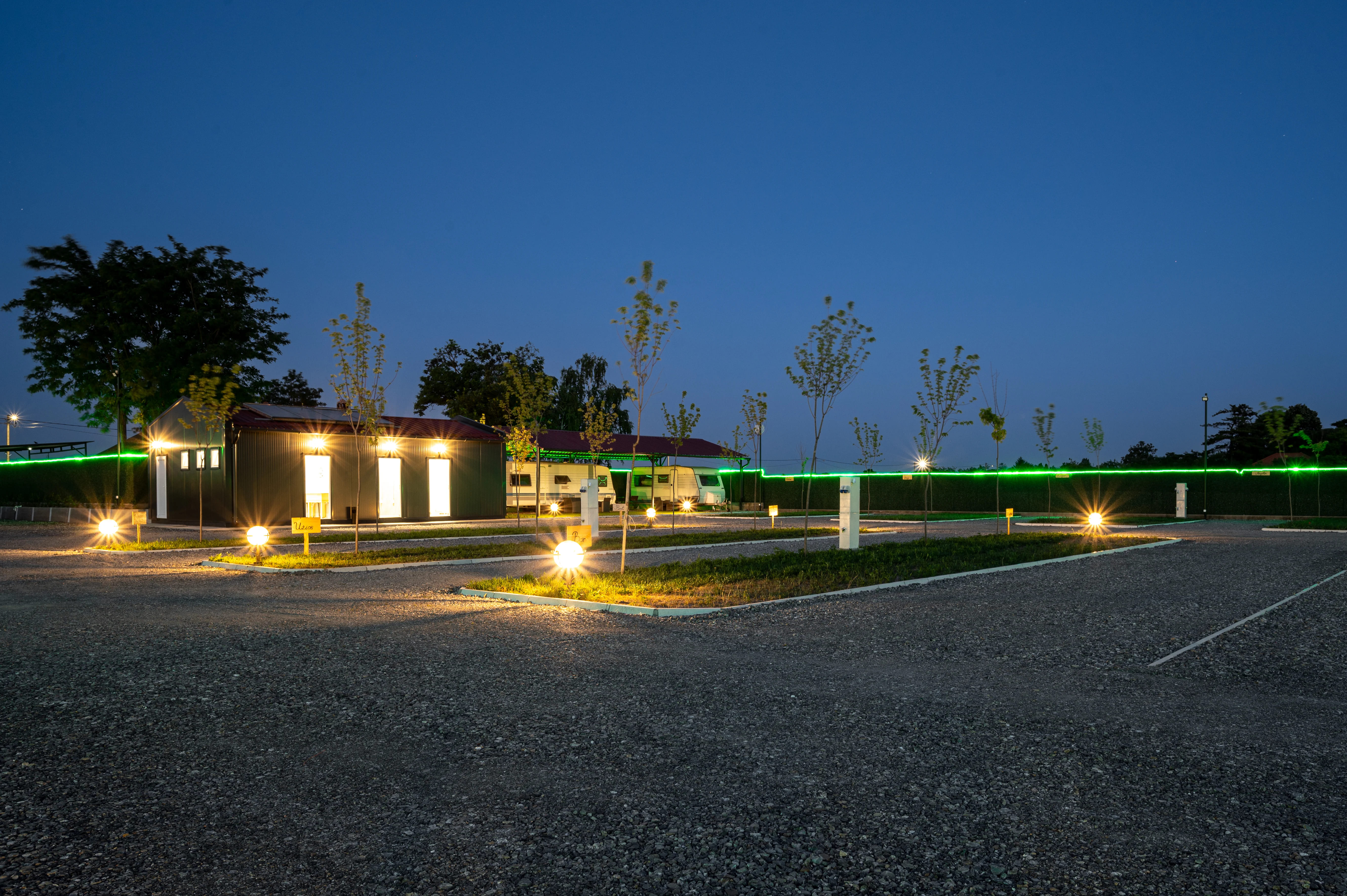 Wohnmobilstellplatz: Night view of Camping Palić - well-lit sanitary block and serviced pitches with electricity, water and young trees. - Camping Palić