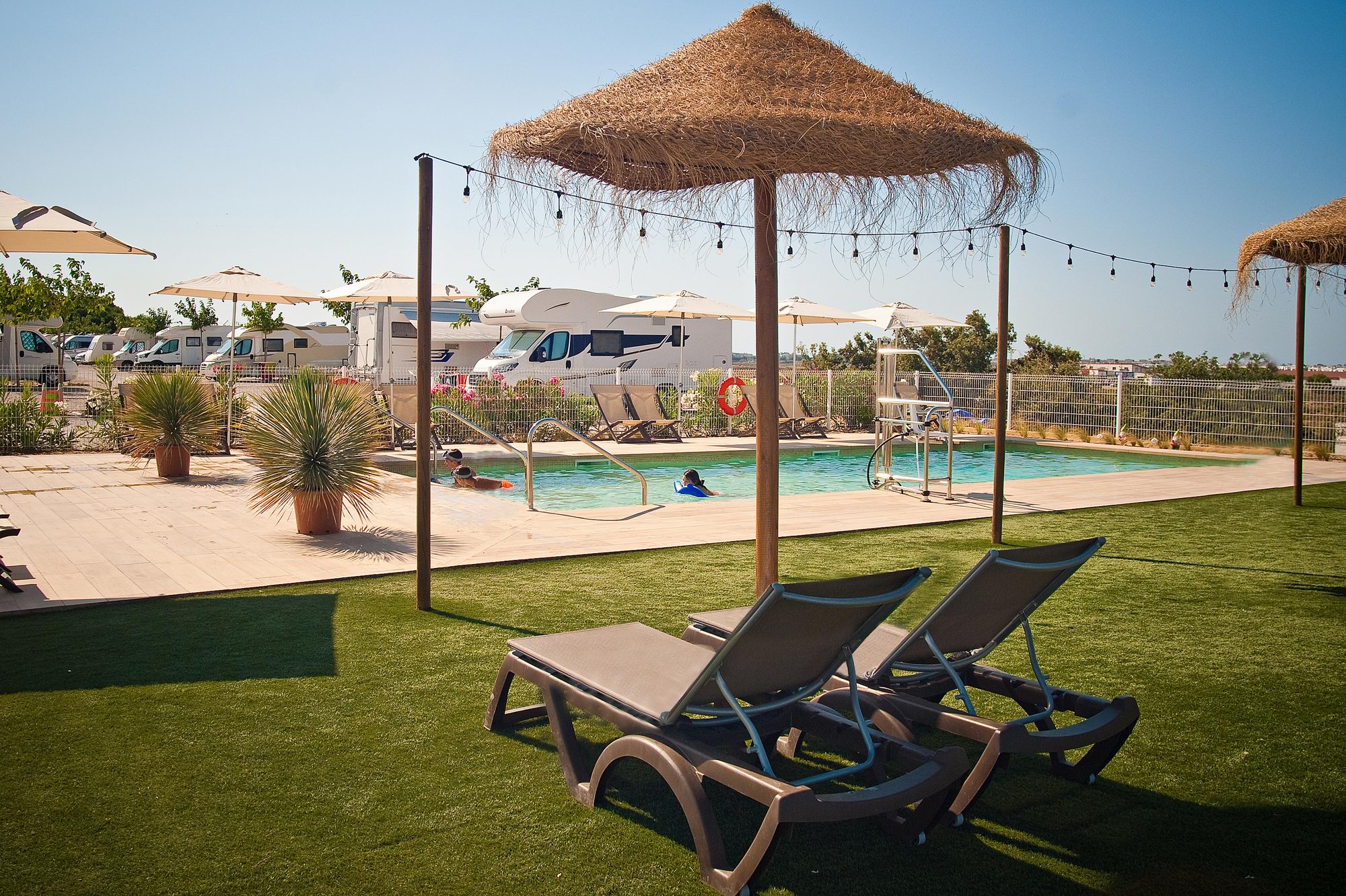 kampeerplaats voor campers - Costa de la Luz - Piscina al aire libre de Camper Park Playas de Luz, abierta durante todo el año, con tumbonas, sombrillas de brezo y zona ajardinada para descansar y disfrutar del clima de la Costa de la Luz. Un espacio de relax para autocaravanistas en Isla Cristina, Huelva, Andalucía. - Camper Park Playas de Luz