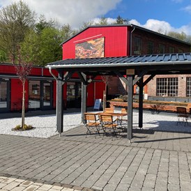 Wohnmobilstellplatz: Der Außenbereich des Cafes, im Hintergrund ist noch ein Teil des Altbaus der alten Hartmann-Industriebrache erhalten und erkennbar.  - Zentrum Via Adrina